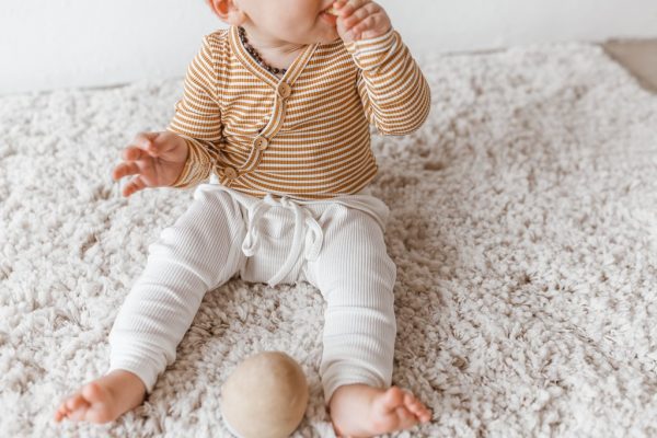 Toddler sitting on fluffy rug in gender neutral clothing