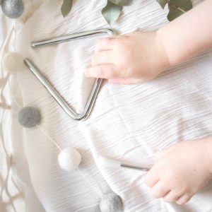 Baby hands holding mini triangle instrument on white cloth and leaves